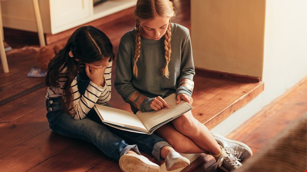 Två barn sitter på golvet och läser en bok tillsammans.