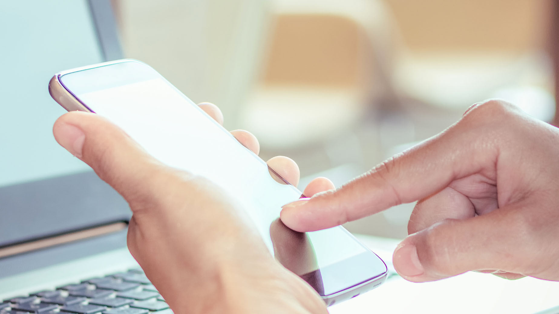 Mobiltelefon i hand, laptop i bakgrund foto Istock