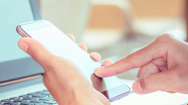 Mobiltelefon i hand, laptop i bakgrund foto Istock